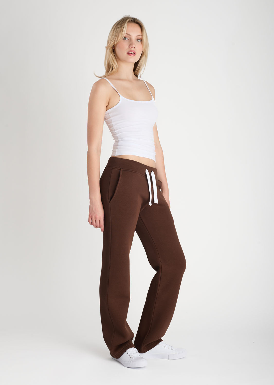 Woman wearing a white tank top and brown sweatpants with white stripes on a white background