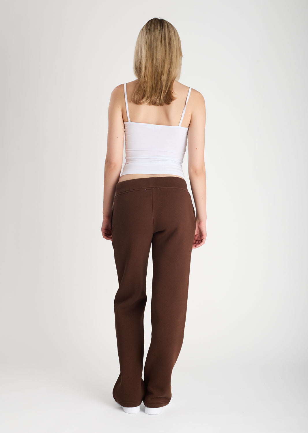Woman wearing brown pants and a white top on a plain background