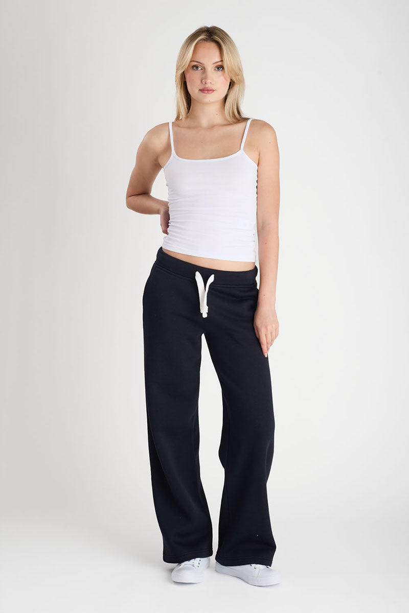 Woman wearing a white tank top and dark navy pants on a white background