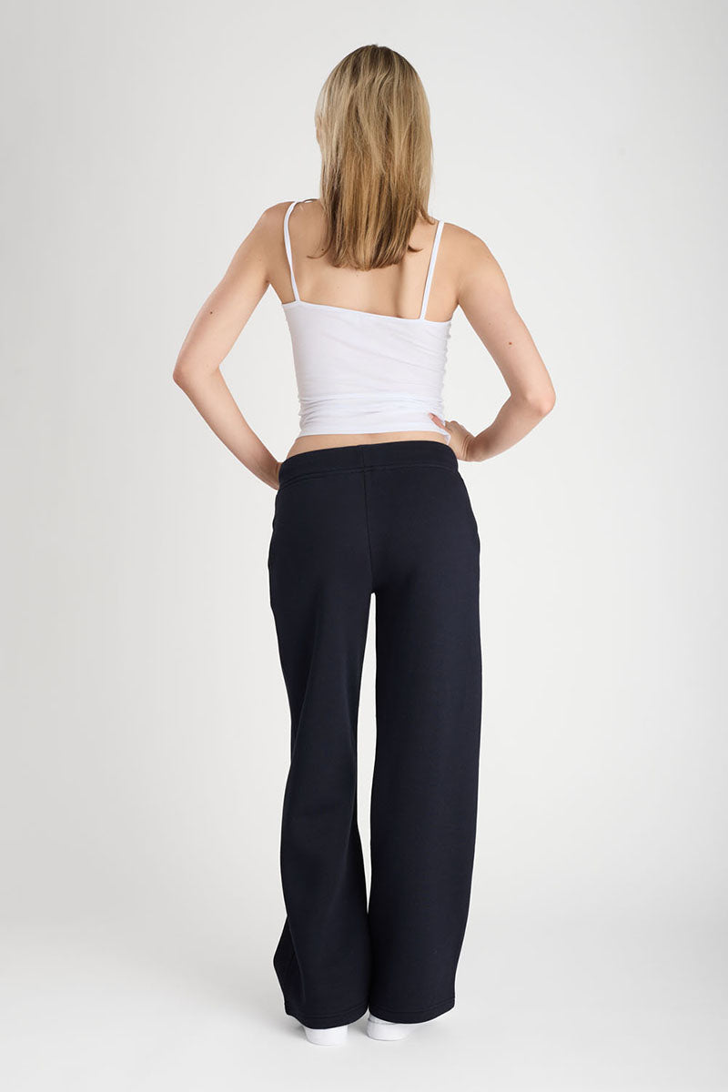 Woman wearing a white crop top and dark navy pants on a plain background