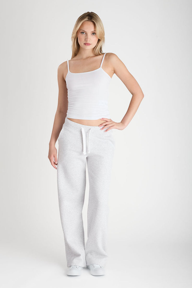 Woman wearing a white tank top and light grey pants on a plain background