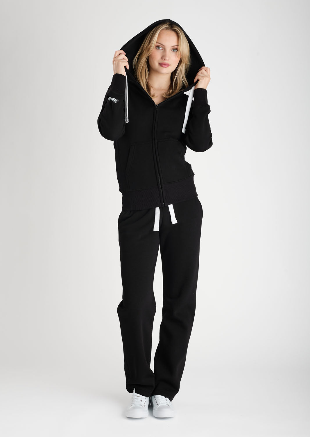 Person wearing a black hoodie and pants with a visible brand logo on a white background