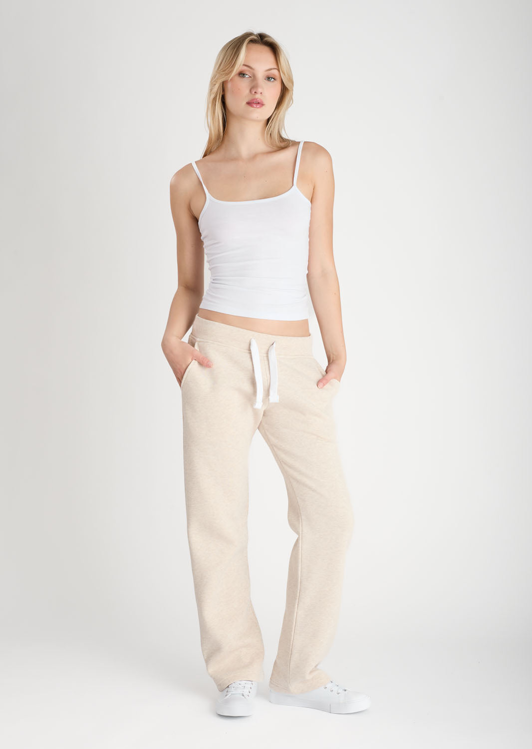 Woman wearing a white tank top and beige pants on a white background