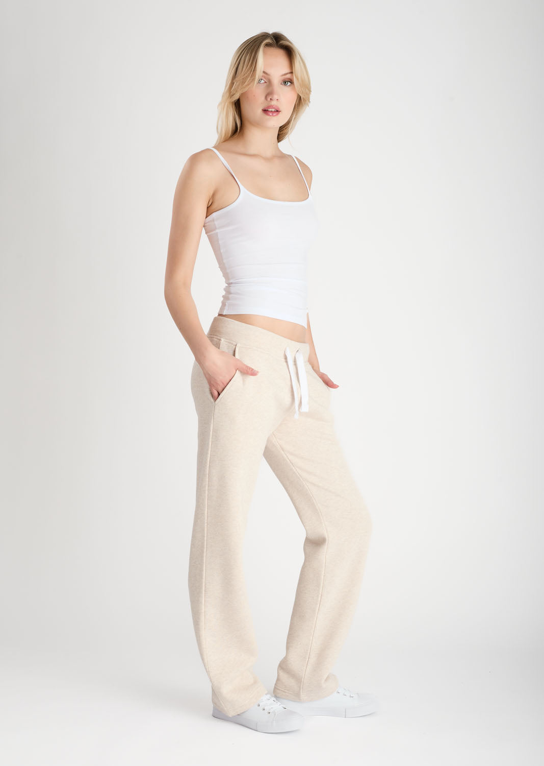 Woman wearing a white top and beige pants on a plain background