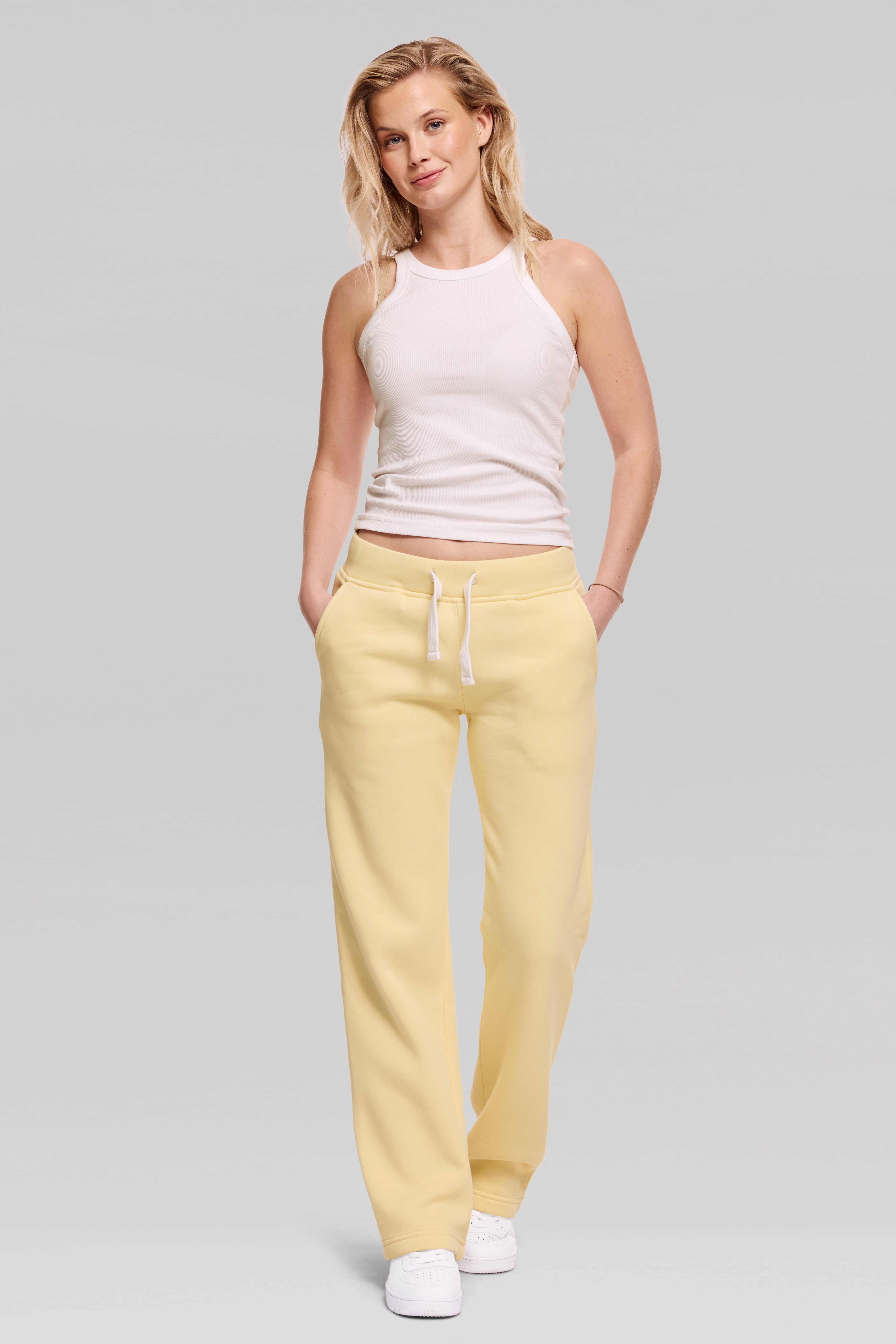 Woman wearing a white tank top and yellow pants on a light gray background